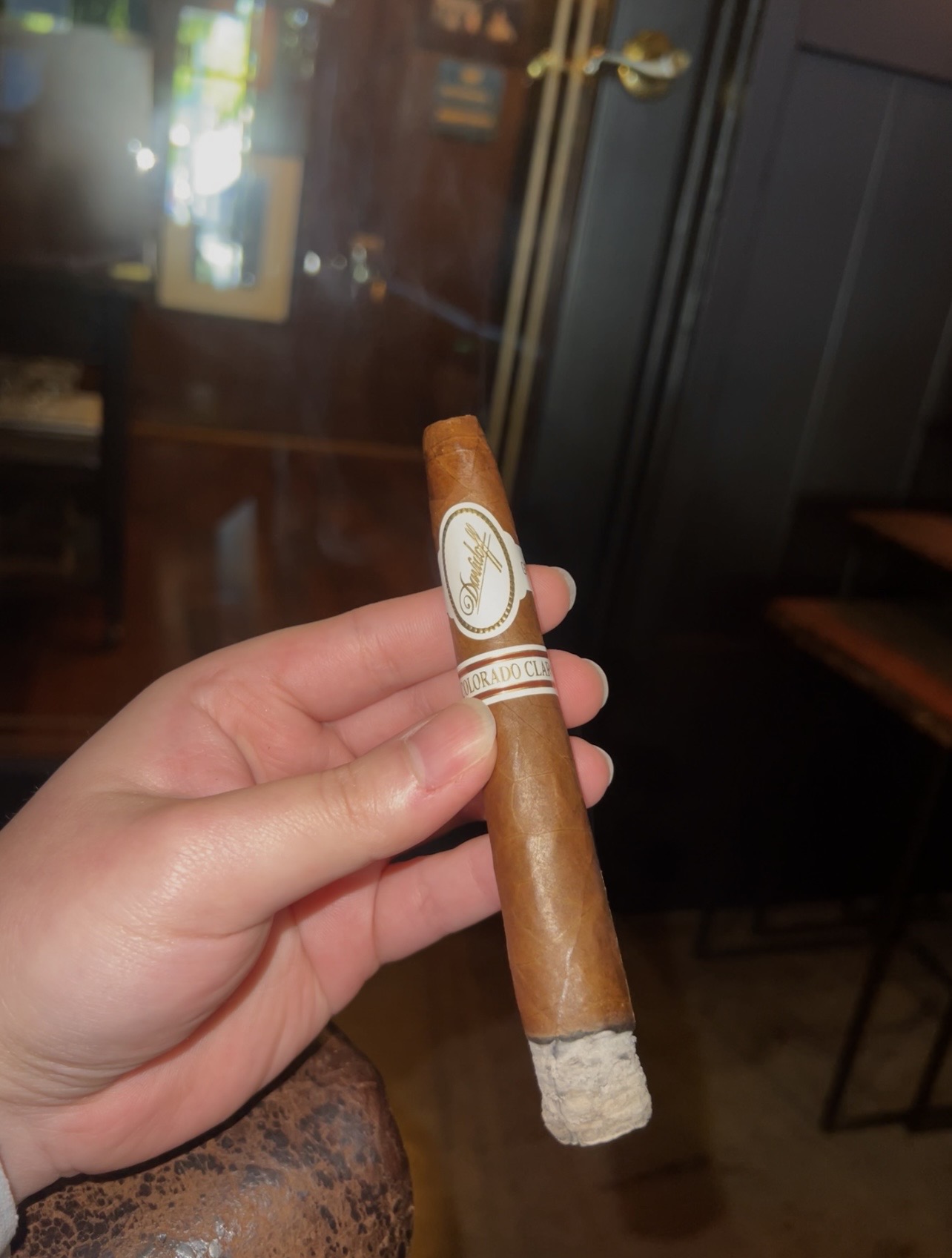 A Davidoff Colorado Claro cigar held in hand, showing its white bands and ash
