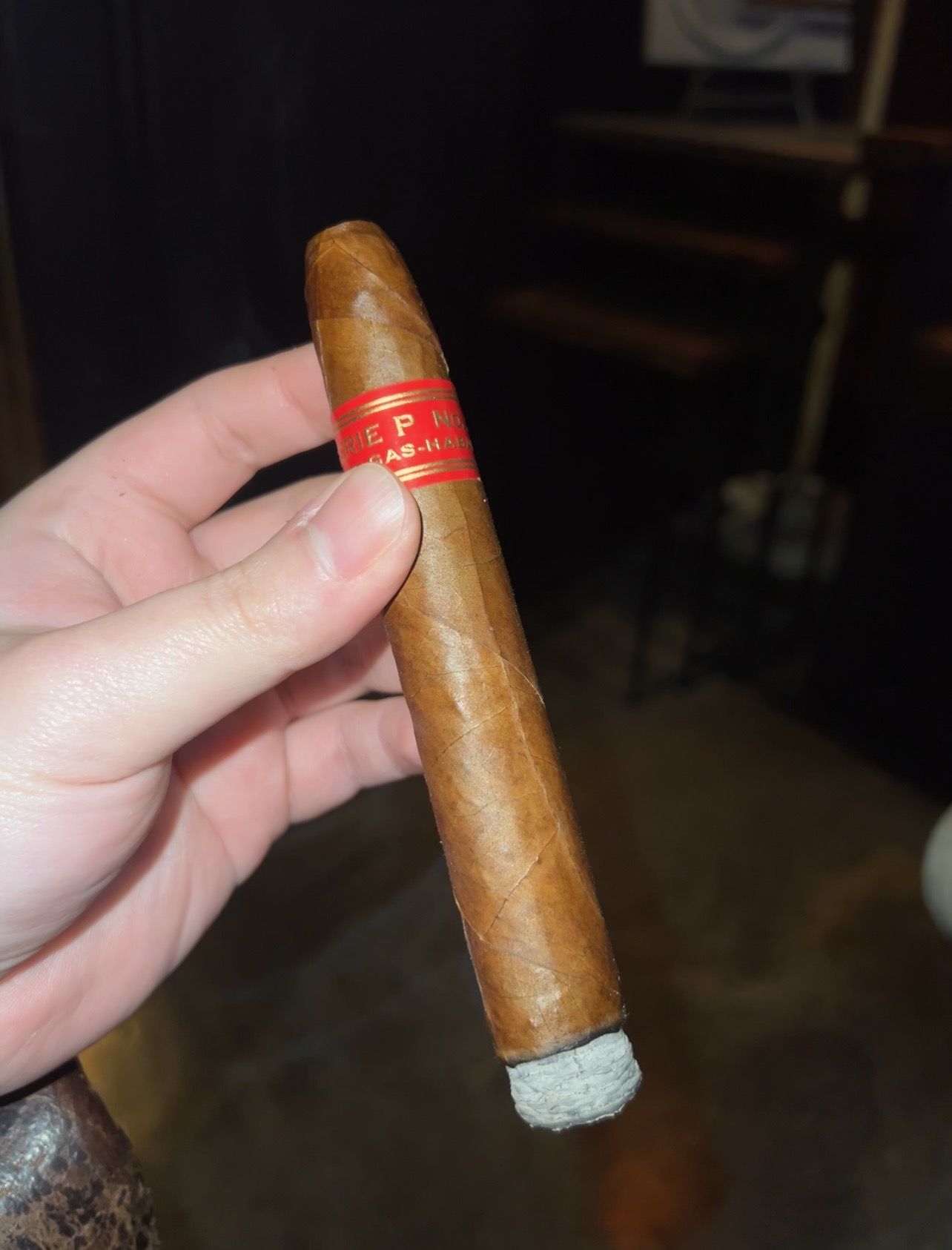A Partagas Series P No. 2 cigar held in hand, showing its red and gold band and ash